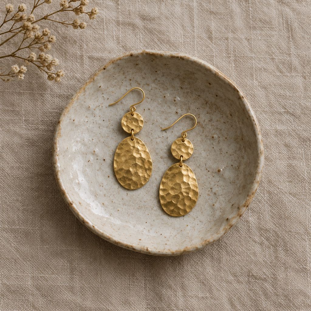 Hammered gold earrings resting on a ceramic dish
